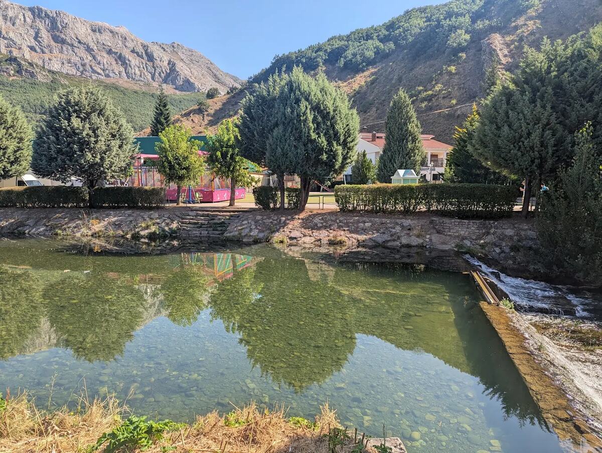 La playa fluvial de Vegacervera: poza del río Torío de agua clara con el fondo de cantos visible, escaleras de piedra para bajar y la montaña caliza detrás, León