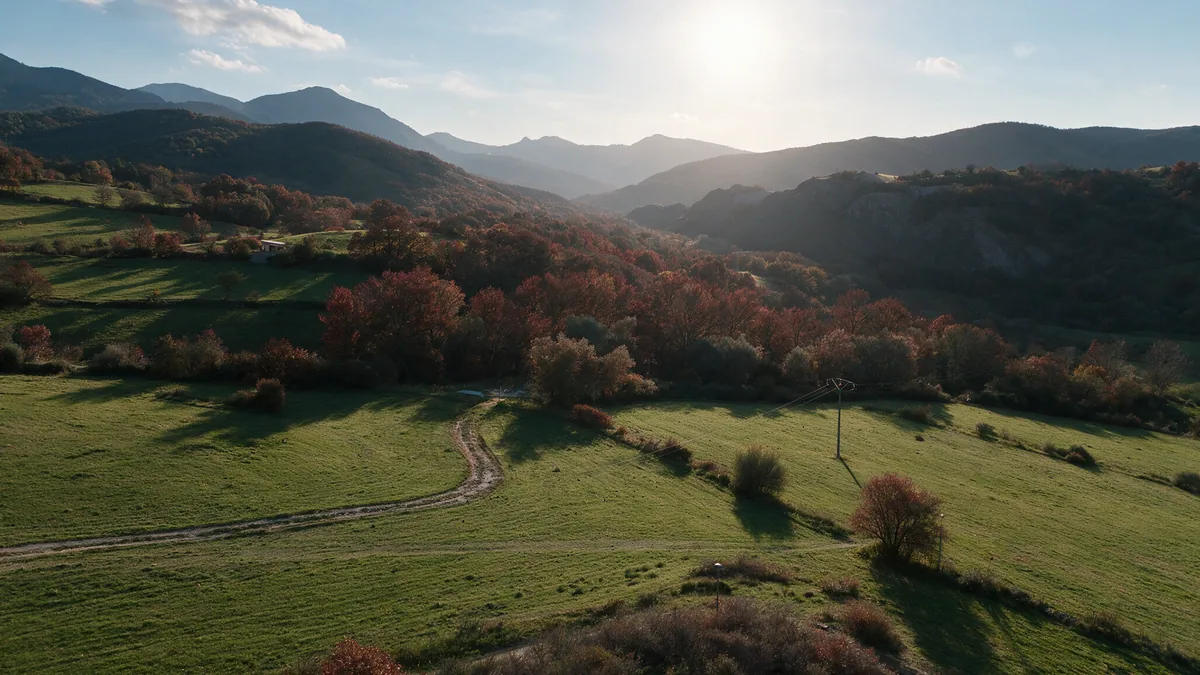 El Valle de Vegacervera en otoño al atardecer, con prados verdes, bosque rojizo y la montaña de León a contraluz