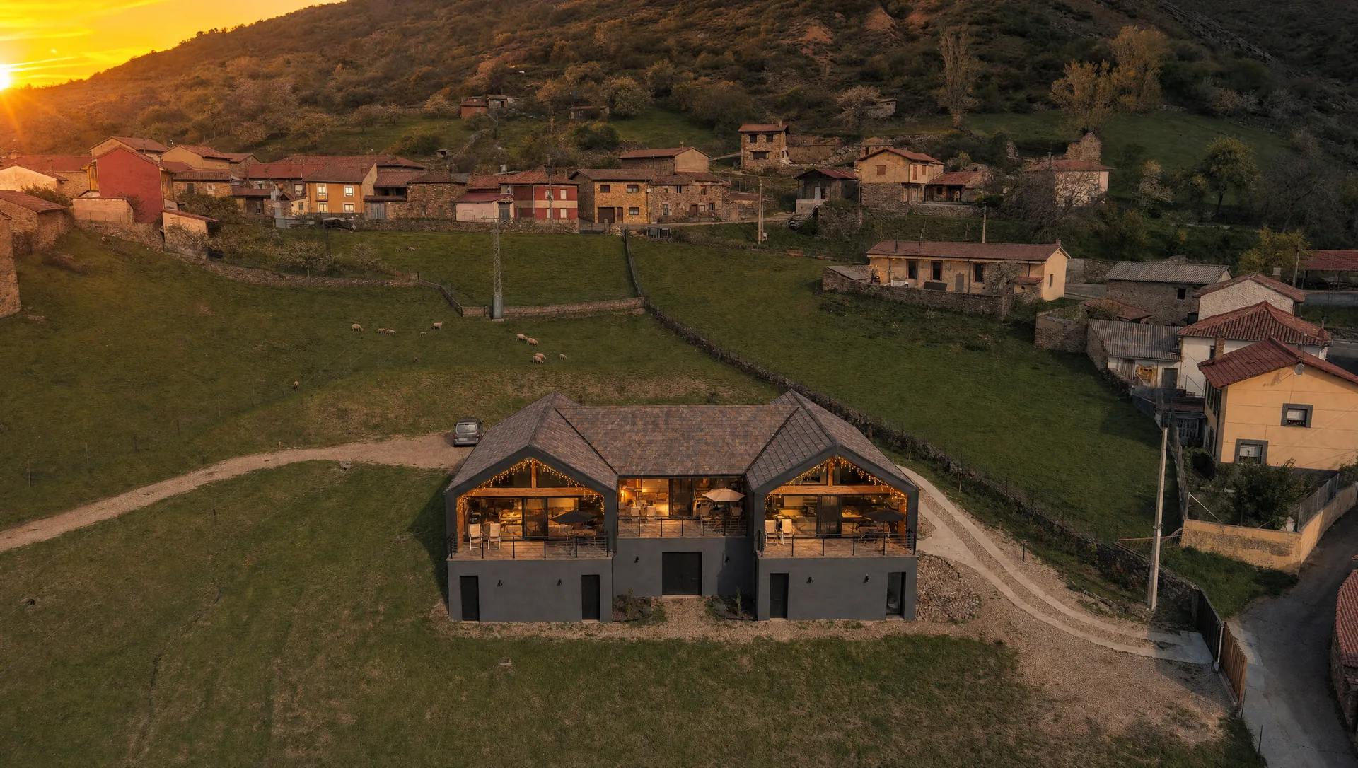 Las tres casas rurales de La Finca del Valle iluminadas al atardecer frente al pueblo de Vegacervera